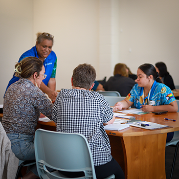 A group of three people sitting at a table listening intently as an instructor explains Blurred Borders Queensland training