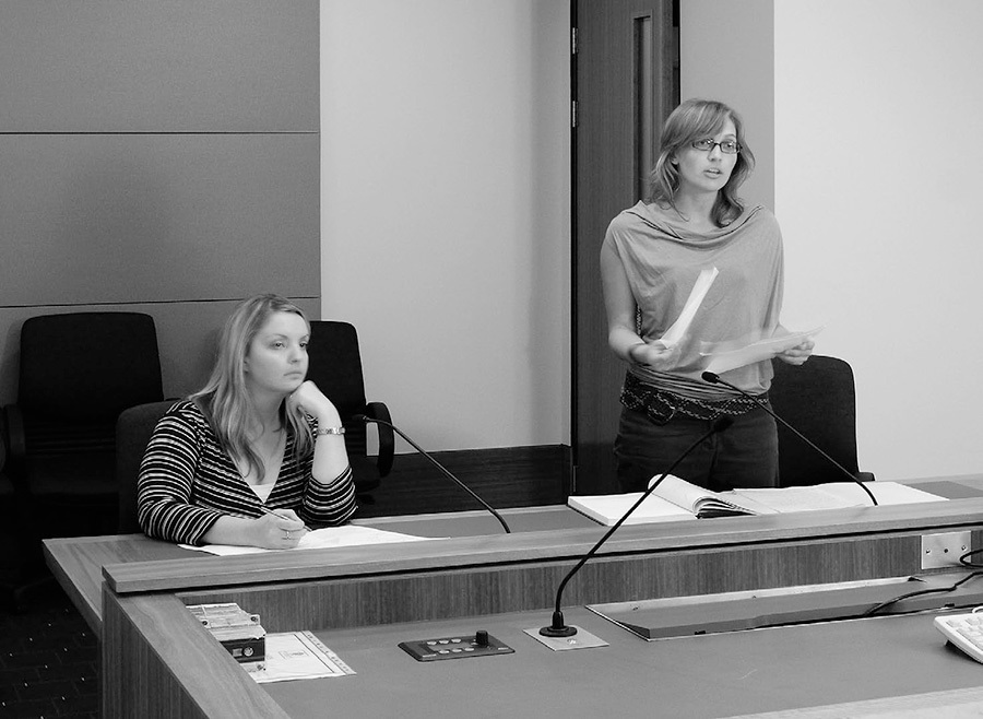 A photo of two women in a courtroom, one is standing, giving evidence.